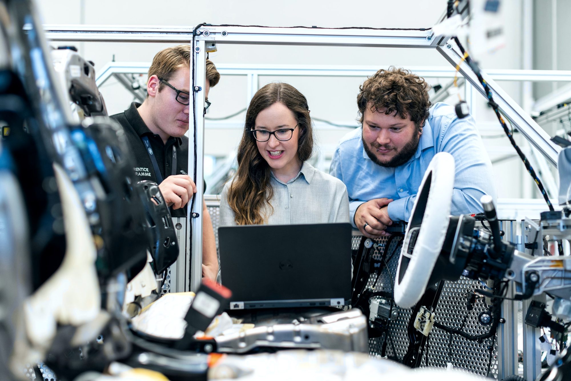 Three engineers working at a laptop beside a robot